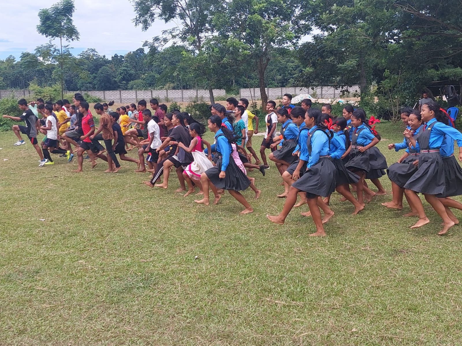 Children practising a running movement drill together on a grass field during the Meghalaya project